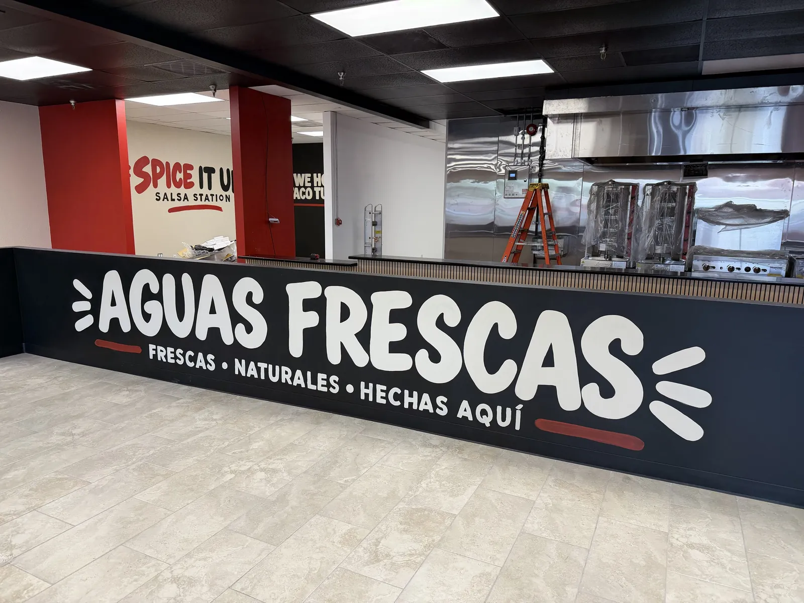 La Flama Taqueria's black order counter painted with Aguas Frescas, with red walls and the salsa station behind