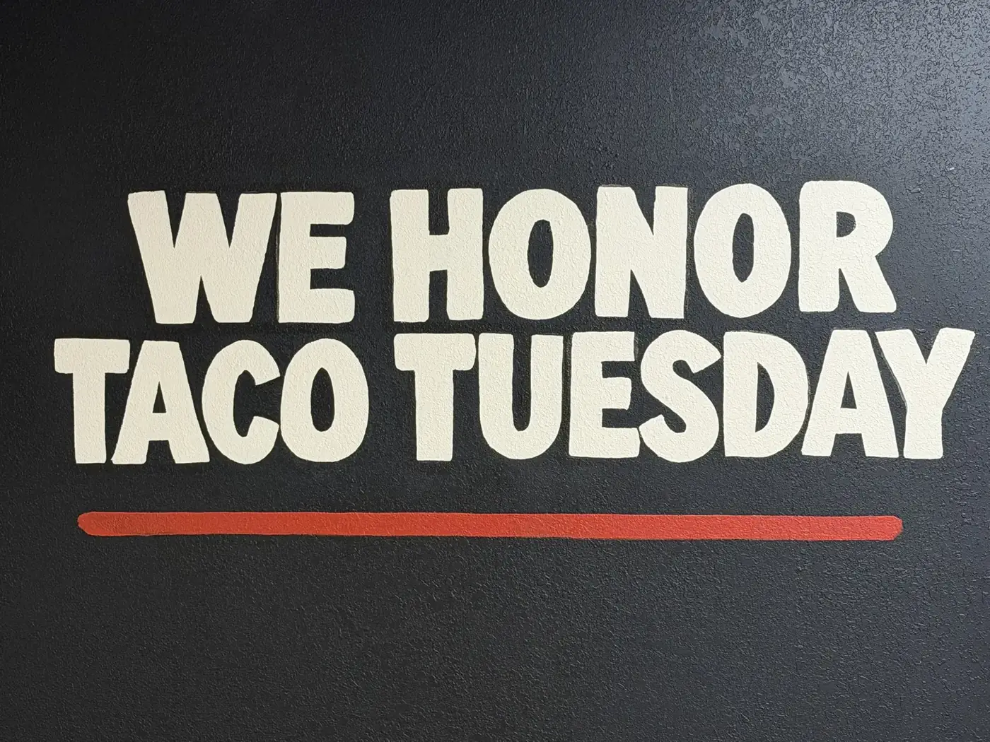 Hand-painted wall inside La Flama Taqueria reading We Honor Taco Tuesday